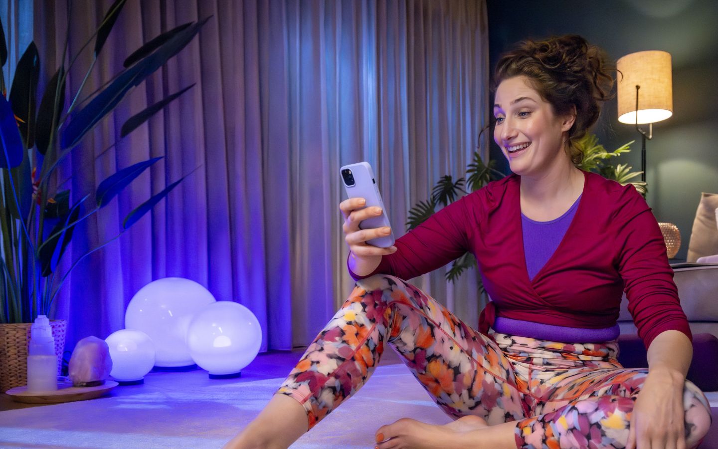 Vrouw zit op de groond en kijkt naar de telefoon tijdens yoga.