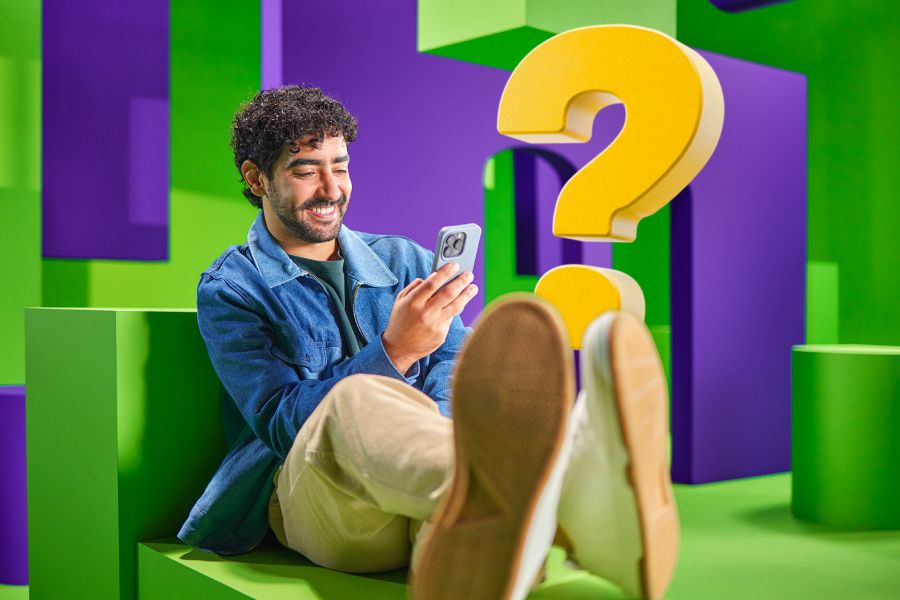 Man ligt op groene bank met telefoon in zijn hand.