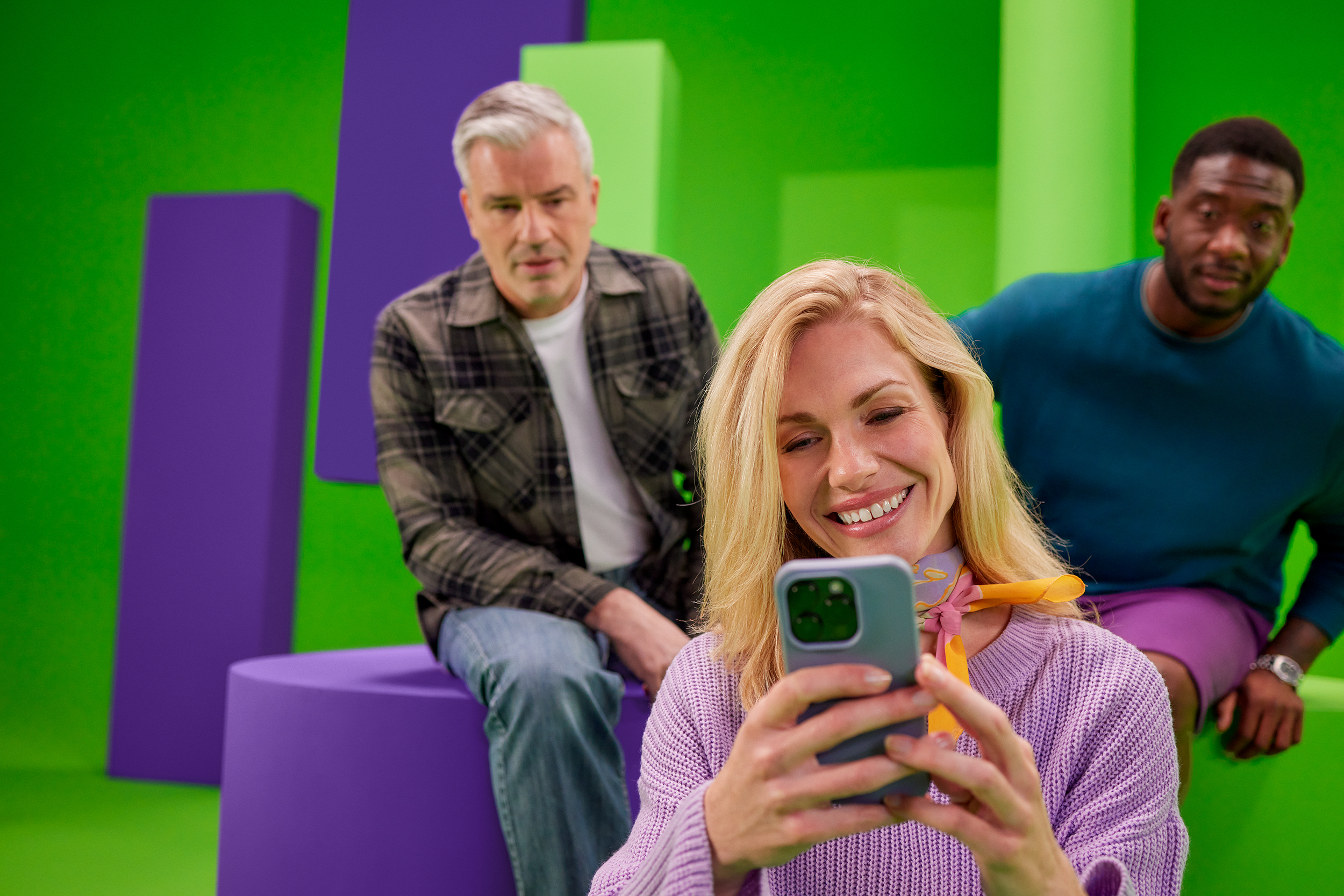 Vrouw kijkt naar het termijnbedrag op haar telefoon. Twee mannen kijken mee.