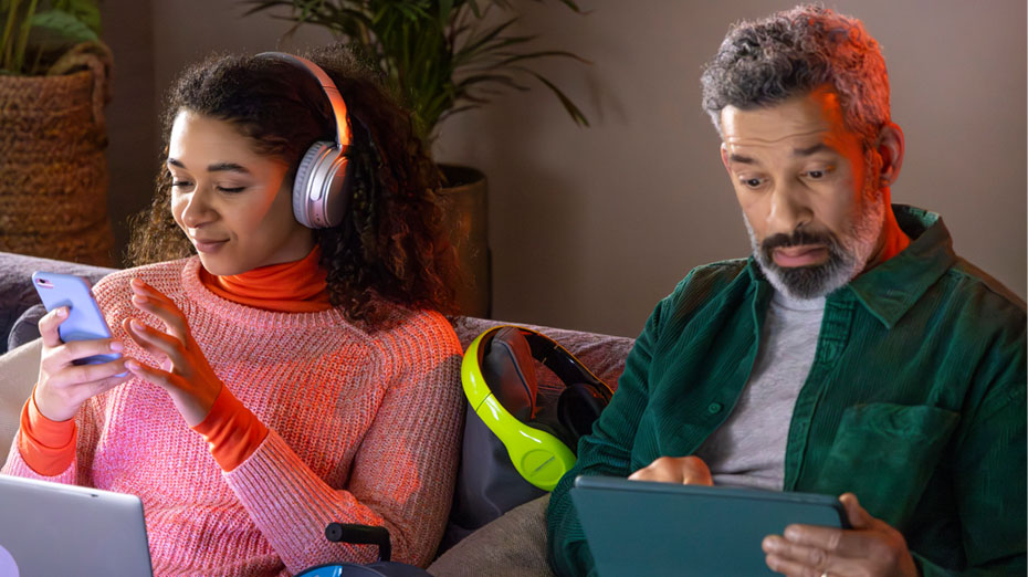Man zit op de bank en kijkt naar zijn iPad. De vrouw naast hem draagt een koptelefoon.